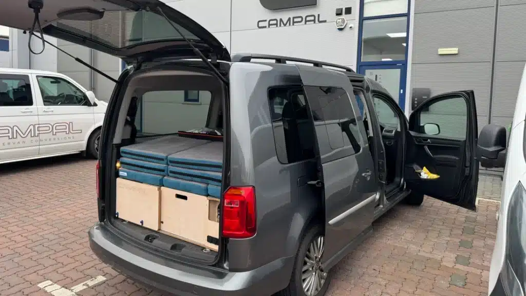 VW Caddy Maxi fitted with Campal Vacation removable camper conversion kit featuring pull-out storage drawers and stacked bed cushions.