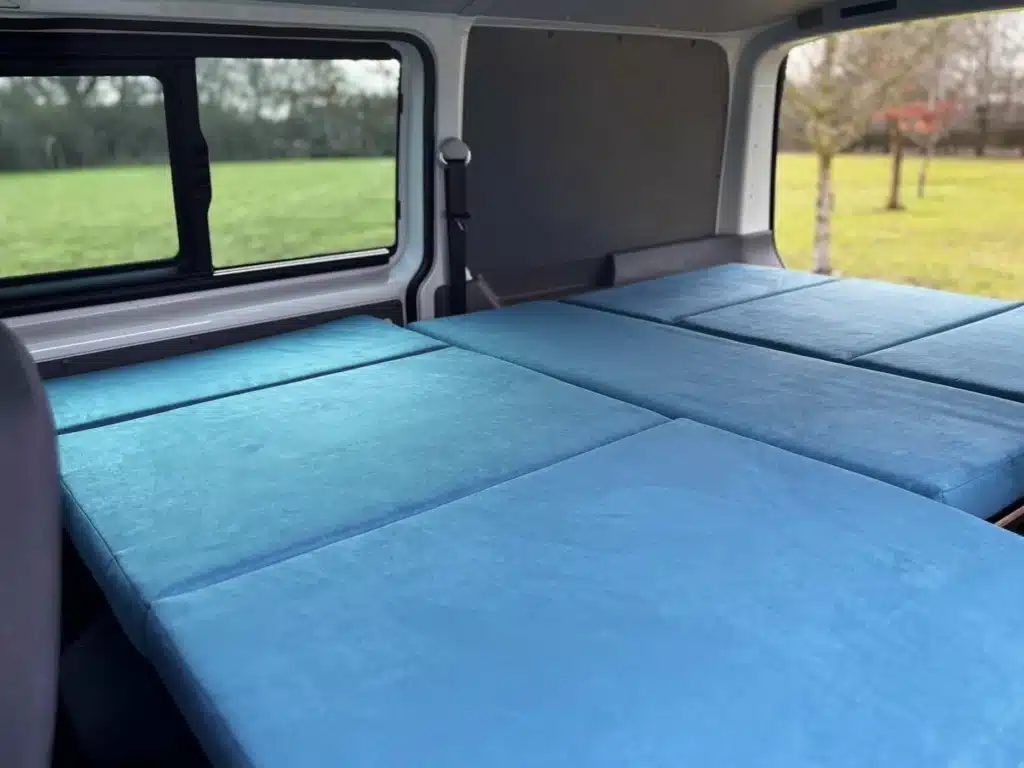 nterior view of a VW Transporter converted with a Campal Elevate kit, showing the flat sleeping surface with blue upholstery.