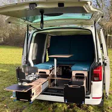 VW Transporter camper conversion by Campal showing the lounge configuration with internal seating, a swivel table, and an extended outdoor cooking station.