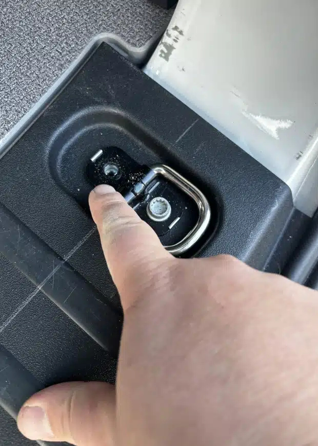 Close-up of a finger pointing to a factory-fitted tie-down anchor point in the VW ID Buzz floor used to secure Campal camper kits without drilling.