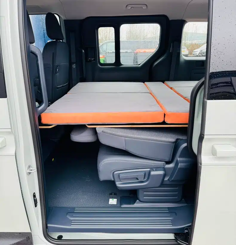 Extended 200cm Campal bed platform deployed over the folded seats of a Kia PV5 electric camper, viewed through the open side door