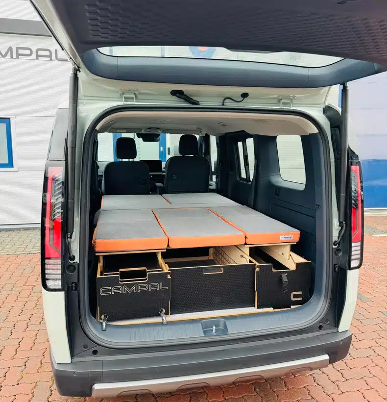 Rear view of the Kia PV5 with the fully extended double bed camper conversion resting on CNC-machined birch plywood boot storage boxes