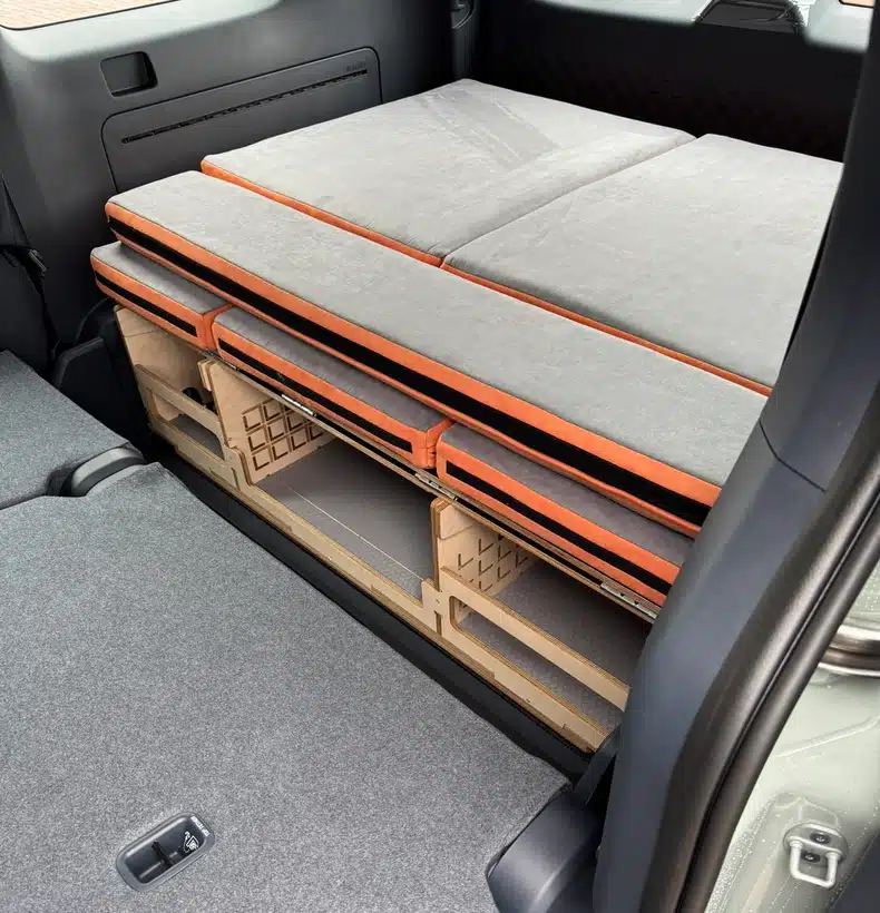 Close-up of the folded Campal camper conversion kit compactly stored in the boot of a Kia PV5, sitting neatly behind the upright rear passenger seats
