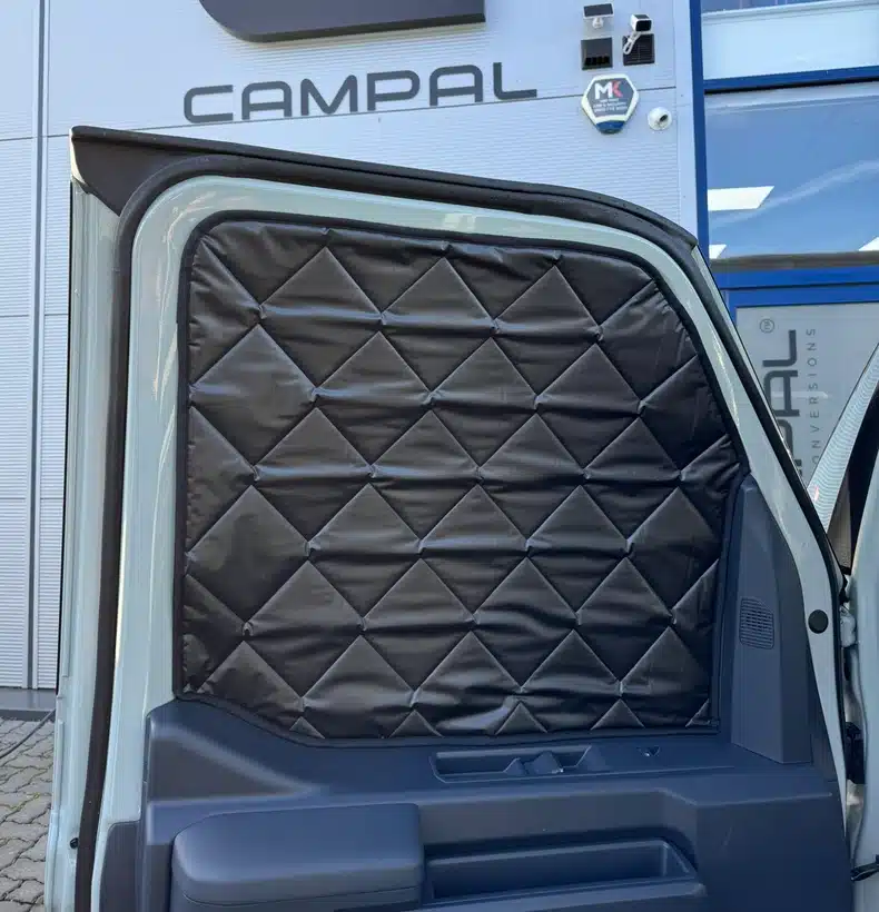 Optional quilted thermal window blinds fitted to the front door of the Kia PV5 camper, designed to insulate the vehicle's large glass areas