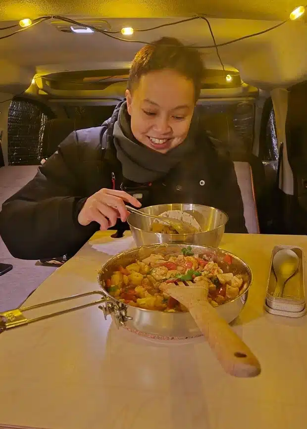 Close-up of a hot meal served on a wooden table inside a Citroën Berlingo micro camper, showing the comfort of the "seat-and-table" layout.