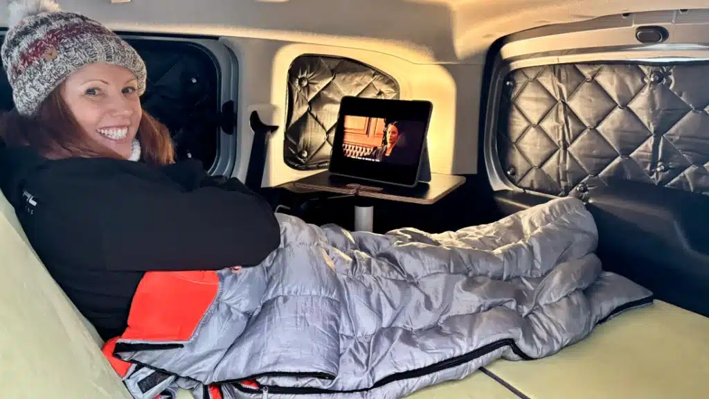 Campal co-founder Lisa while relaxing in a sleeping bag on a full-width Berlingo camper bed, featuring insulated window covers for privacy and warmth.
