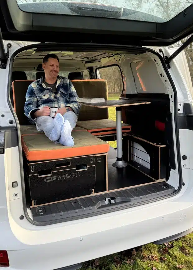 Man relaxing with a coffee inside a VW ID Buzz camper using the Campal dining table and seating configuration to demonstrate interior headroom.