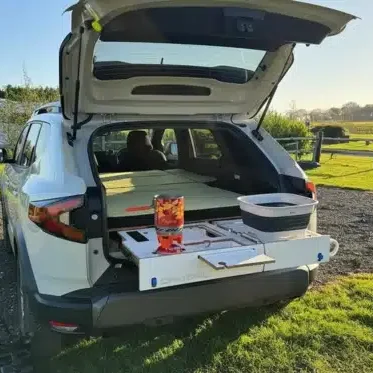 Campal removable camper conversion kit for SUVs featuring a pull-out birch plywood kitchen with stove and sink, set up in a vineyard.