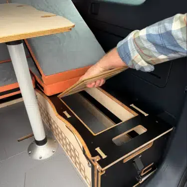 Person lifting the precision-engineered birch plywood lid of the Campal seating unit to access the generous internal storage space