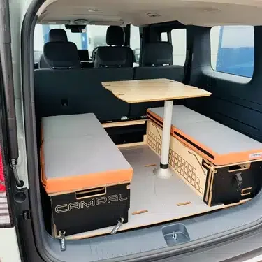 Classic two-bench seating arrangement with a central dining table installed seamlessly in the boot of a Kia PV5 behind the upright passenger seats